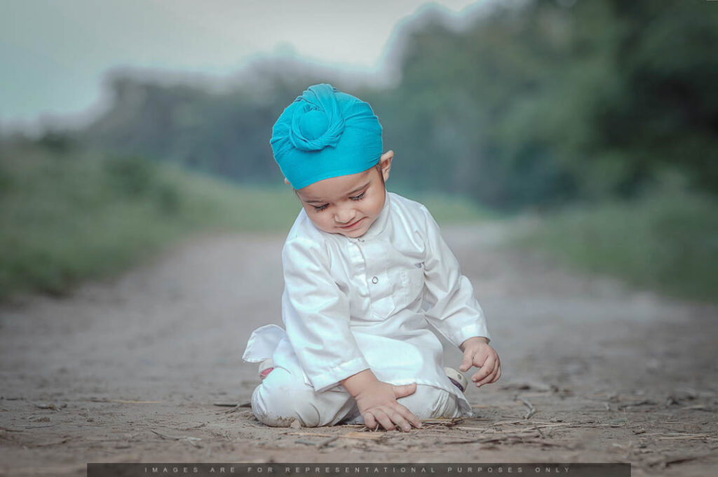 Little boy in a white kurta and blue turban playing on a dirt path outdoors.